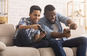 teenage black male playing video games with his adoptive father, laughing