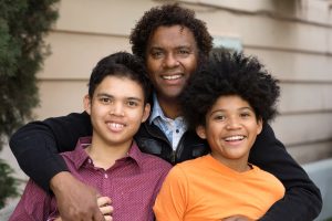 A father with his arms around his two sons. They are all smiling.