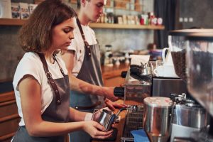 Young female barista working at a coffee shop making a cup of coffee.