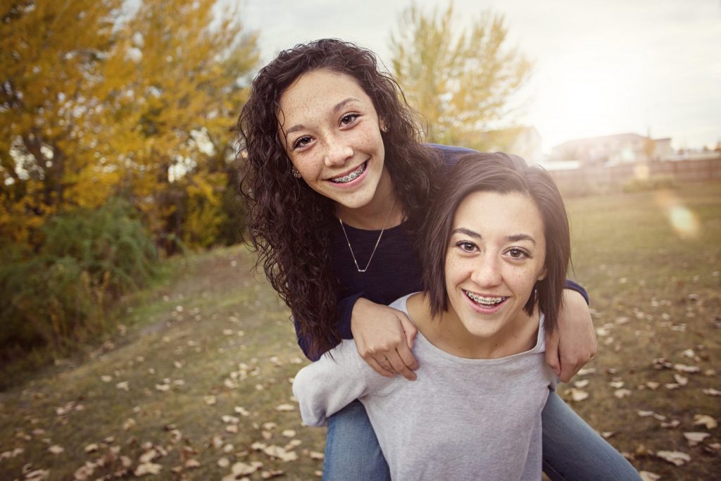 Cute hispanic teenage girls playing together outdoors during a warm fall day. Sun flare in the background. The one girl is giving the other girl a piggy back ride.