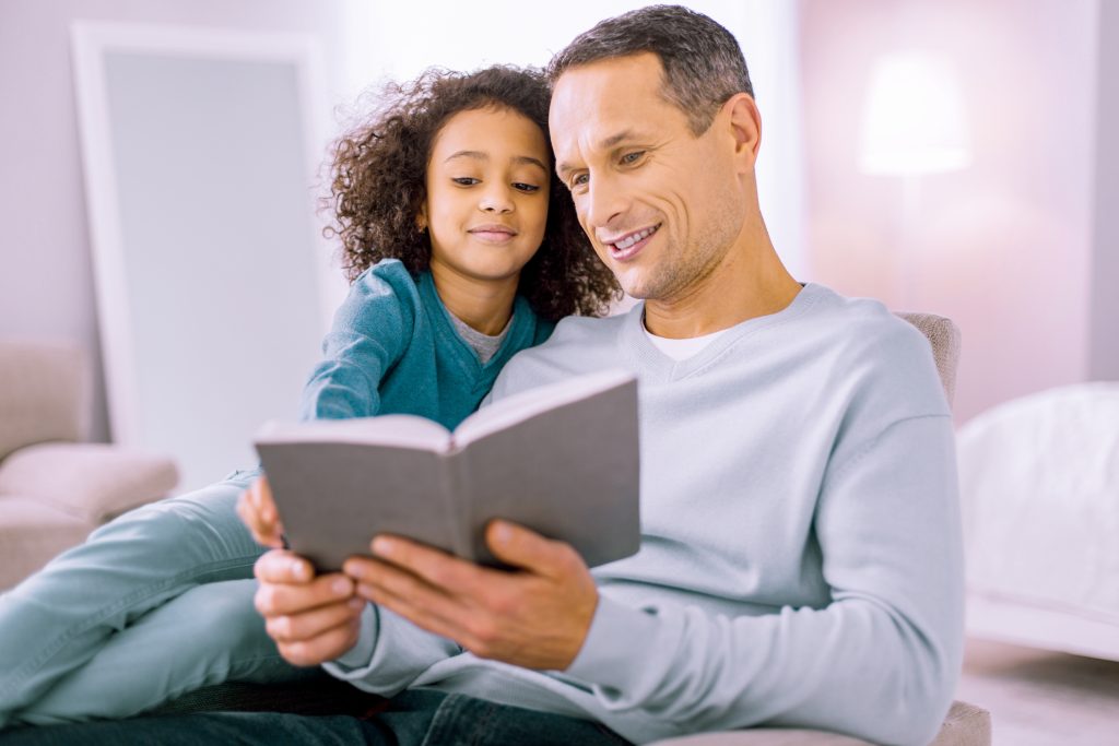 A father reading a bedtime story to his adopted daughter.